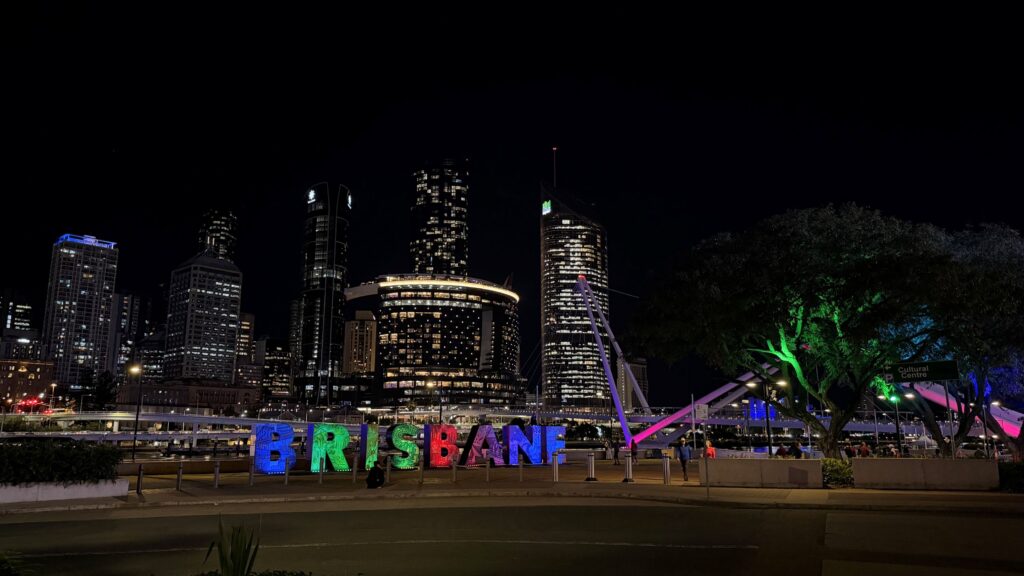 Colorful illuminated "BRISBANE" sign in front of the city skyline at night.