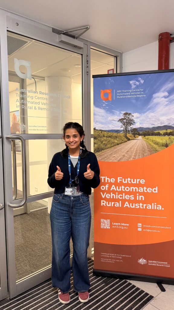 Smiling Iris Jestin giving two thumbs up beside a banner.