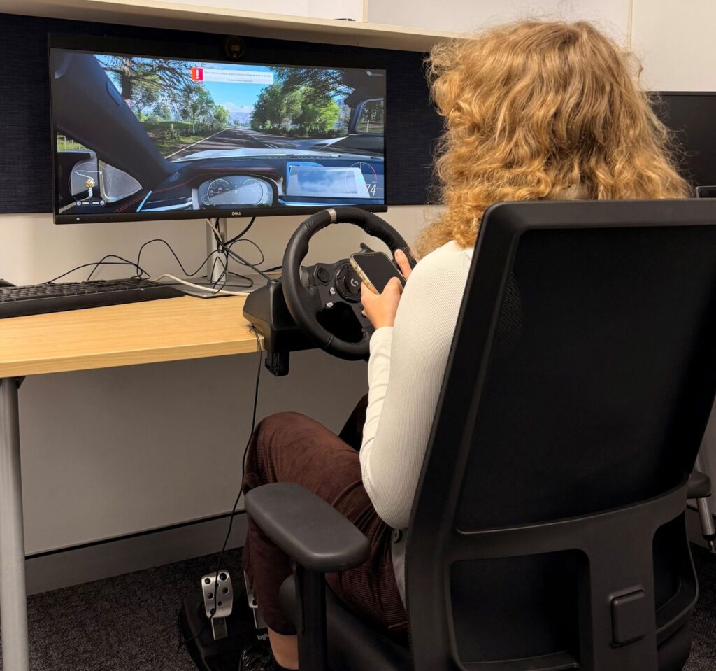 Woman seen from behind holding a phone while using a driving simulator.